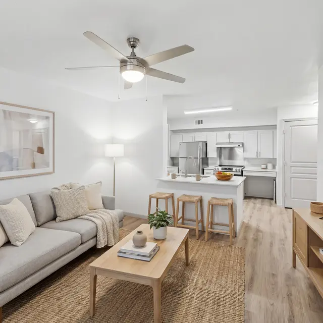 A living room with a grey couch, a wooden table, and a ceiling fan.